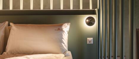 A bedroom with a bed, pillows, a wall-mounted light, and a power outlet.