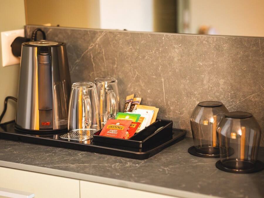 A kitchen counter with a coffee maker, four glass tumblers, a tray with Twinings English Breakfast tea bags, and two glass carafes.