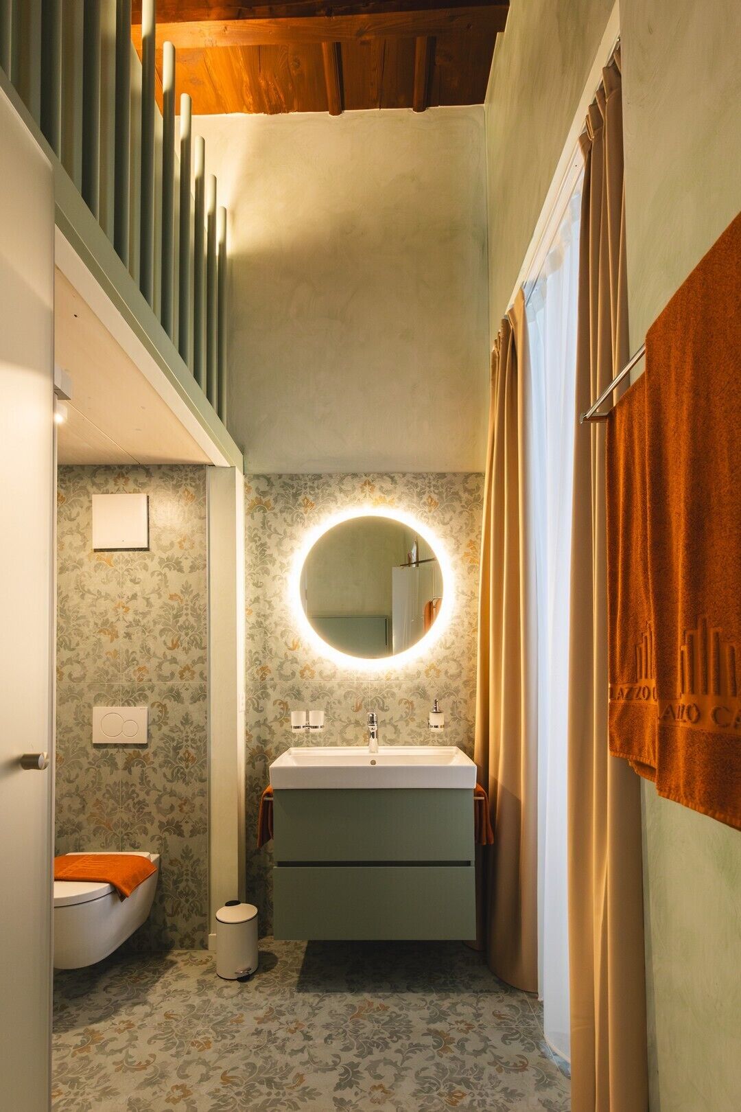 Ein Badezimmer mit einem runden Spiegel, zwei Waschbecken, einer Toilette und einem Mülleimer.