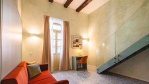 A room with a red sofa, a small table with a chair, a painting on the wall, and a staircase with glass railings. - Palazzo Canetti Locarno (Locarno)