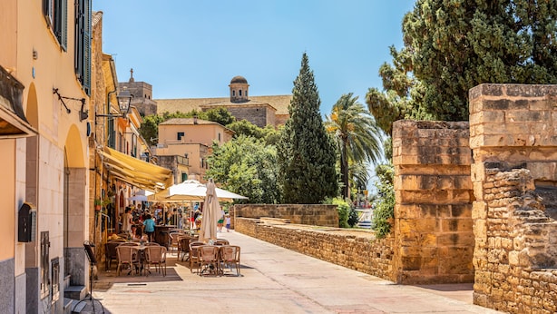 A narrow street with outdoor seating, stone walls, and traditional buildings.