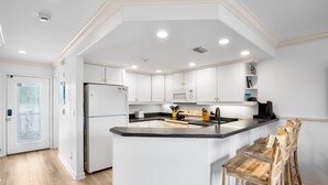 A modern kitchen with white cabinetry, a central island, and a dining area with wooden chairs.