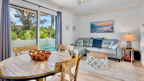 A room with a dining table, chairs, a sofa, a coffee table, a ceiling fan, a painting, and a lamp.