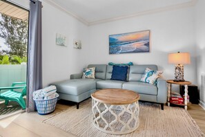 A living room with a grey sofa, a round wooden coffee table, a lamp, and a painting of a beach scene.