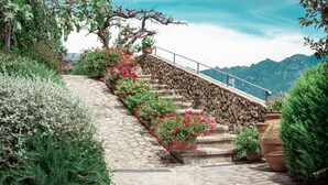 Una escalera de piedra con macetas y flores, que sube una colina con vista a la montaña al fondo.