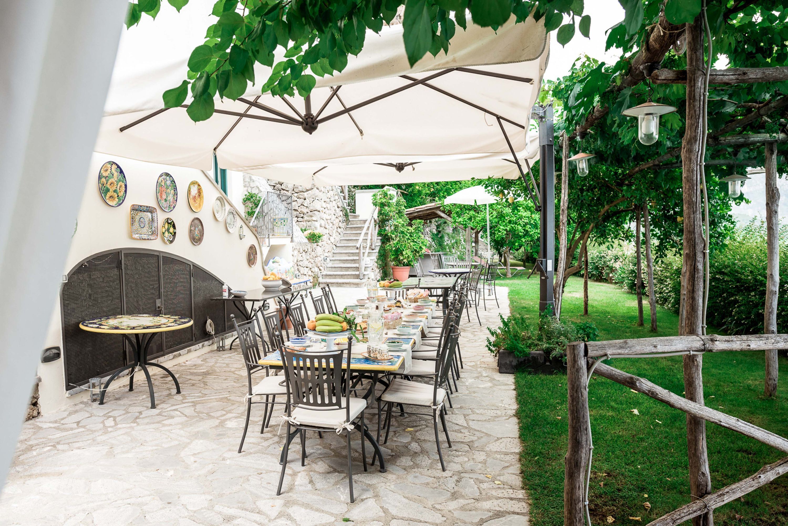Un espace extérieur aménagé pour les repas, avec des tables et des chaises, un sol en pierre et une vue sur le jardin.