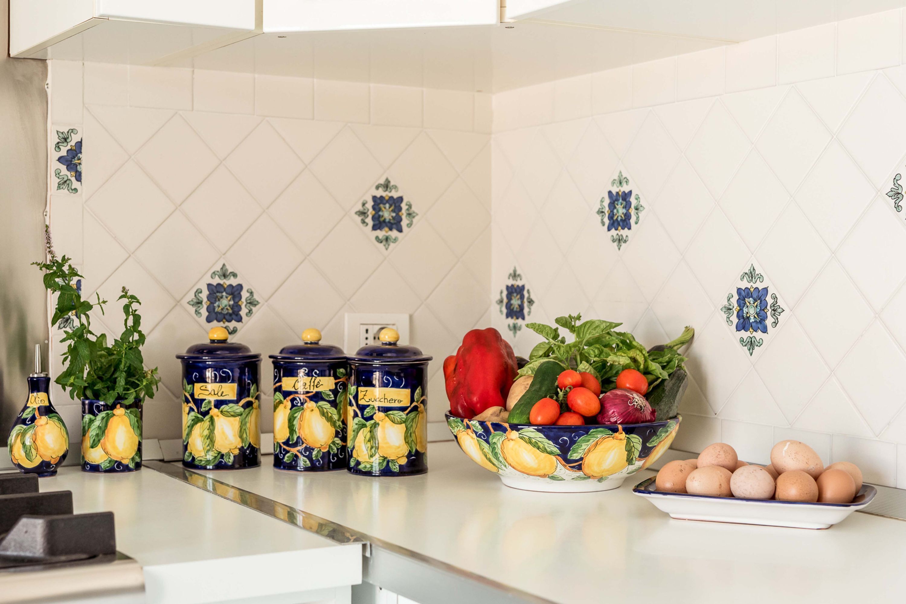 A kitchen counter with decorative ceramic containers, a bowl of fresh produce, and a plate of eggs.