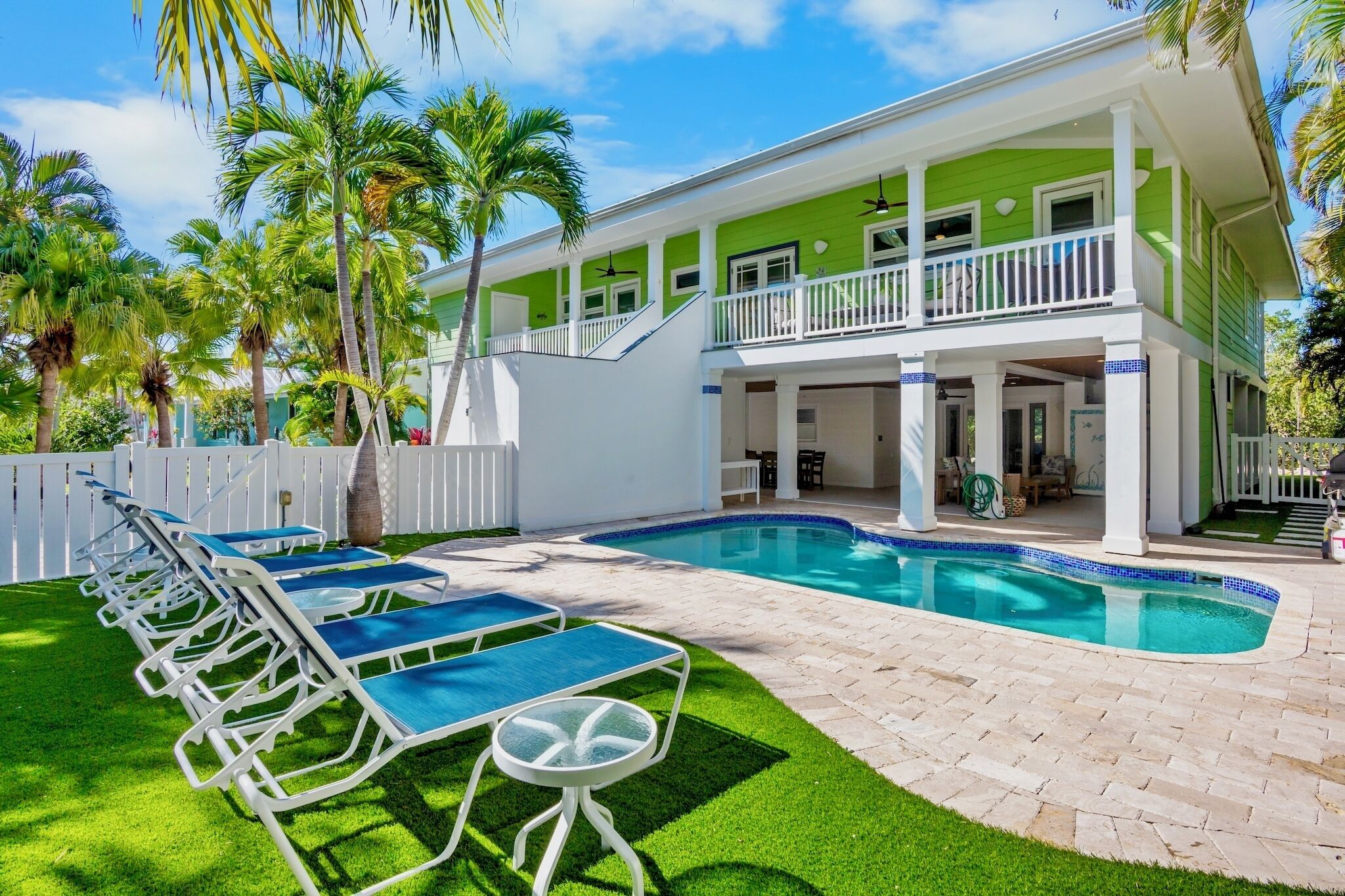 A two-story house with a swimming pool, outdoor furniture, and palm trees.