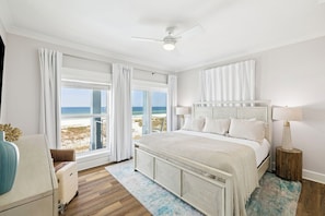 A bedroom with a large bed, a ceiling fan, a view of the beach, and a window with white curtains. - Gulf Views! Private Pool Overlooking the Gulf! Elevator! (Mexico Beach)