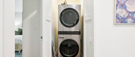 A laundry room with two stacked front-loading washing machines, a door leading to another room, and a painting on the wall.