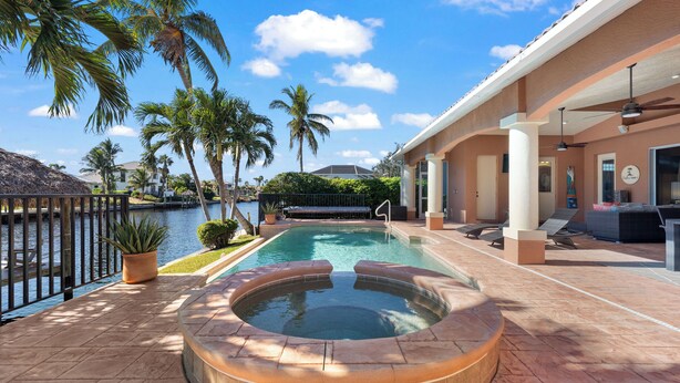 A pool area with a hot tub, lounge chairs, and a view of the water.