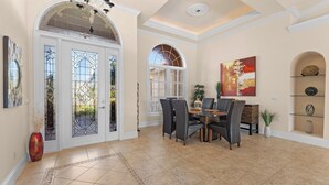 A dining area with a table and chairs, a chandelier, and a large window with decorative glass panels.