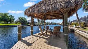 A wooden deck with a thatched roof pavilion, wooden chairs, and a table.