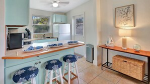 A kitchen with a central island, bar stools, a small refrigerator, and a wall-mounted lamp.