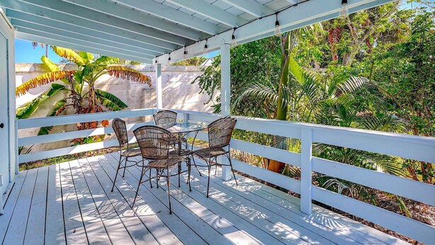 A covered outdoor area with a table and chairs, surrounded by white railings and lush greenery.