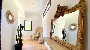 A hallway with a large ornate mirror, a cactus plant, wicker furniture, and a framed picture on the wall.