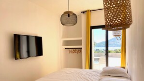 A bedroom with a bed, a TV mounted on the wall, and a view of the outdoors through a window.