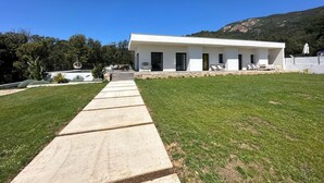 A modern white building with a stone pathway leading to it, surrounded by a well-maintained lawn and a mountain in the background.