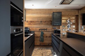 A modern kitchen with wooden wall paneling, a built-in oven, and a flat-screen TV mounted above the counter. - ✨ Le Refuge des 3 Oursons – 14 p. - with Swim Spa, Sauna (Gérardmer)