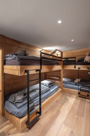 Ein Schlafraum mit Etagenbetten, Holzvertäfelung an Wänden und Boden, einer Deckenleuchte und einem Stofftier im oberen Bett.