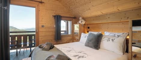 A wooden cabin room with a bed, a window, and a balcony.