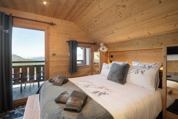 A wooden cabin room with a bed, a window, and a balcony.