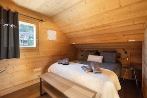 A wooden cabin bedroom with a bed, bench, and window.