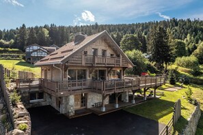 Ein Chalet mit Balkon, Stein Fundament und Blick auf einen bewaldeten Bereich.