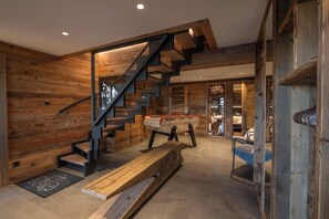 A wooden interior with a staircase, a foosball table, and a bench.