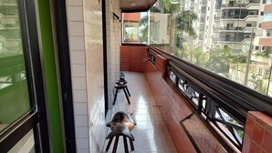Un balcon doté d’un sol carrelé, d’un petit tabouret et d’une fenêtre donnant sur un paysage urbain.