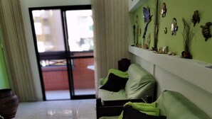 Un canapé vert avec des coussins noirs, un sol carrelé, un rideau et un mur orné de divers objets décoratifs.