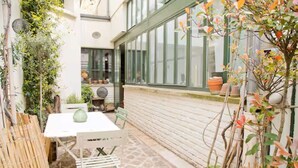 A small patio area with a table and chairs, surrounded by potted plants and a bamboo fence.