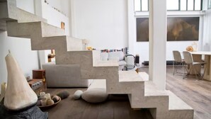 A modern interior with a unique concrete staircase, a sofa, and a dining area.