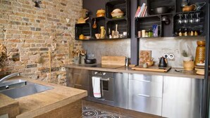 A modern kitchen with a brick wall, stainless steel appliances, and open shelving with kitchenware.