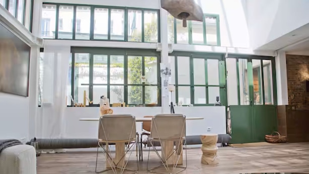 A spacious room with large windows, a dining area with chairs, a table, and a glass-top coffee table.