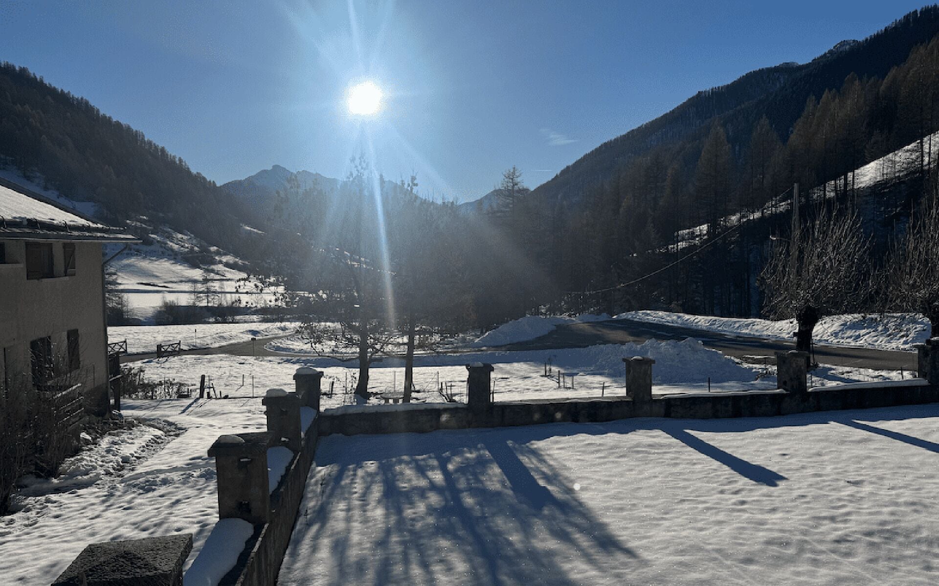 Un paysage enneigé avec une montagne en arrière-plan et un bâtiment sur la gauche.