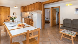 A kitchen with wooden cabinets, a dining table set for four, and a small seating area with a sofa and a table with a newspaper. - Gites Simond welcomes you to Arvieux in the heart of the Queyras Regional Park, (Arvieux)