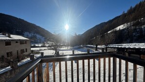 A snowy mountain landscape with a sunlit sky, a wooden deck, and a building with a snow-covered roof. - Gites Simond welcomes you to Arvieux in the heart of the Queyras Regional Park, (Arvieux)