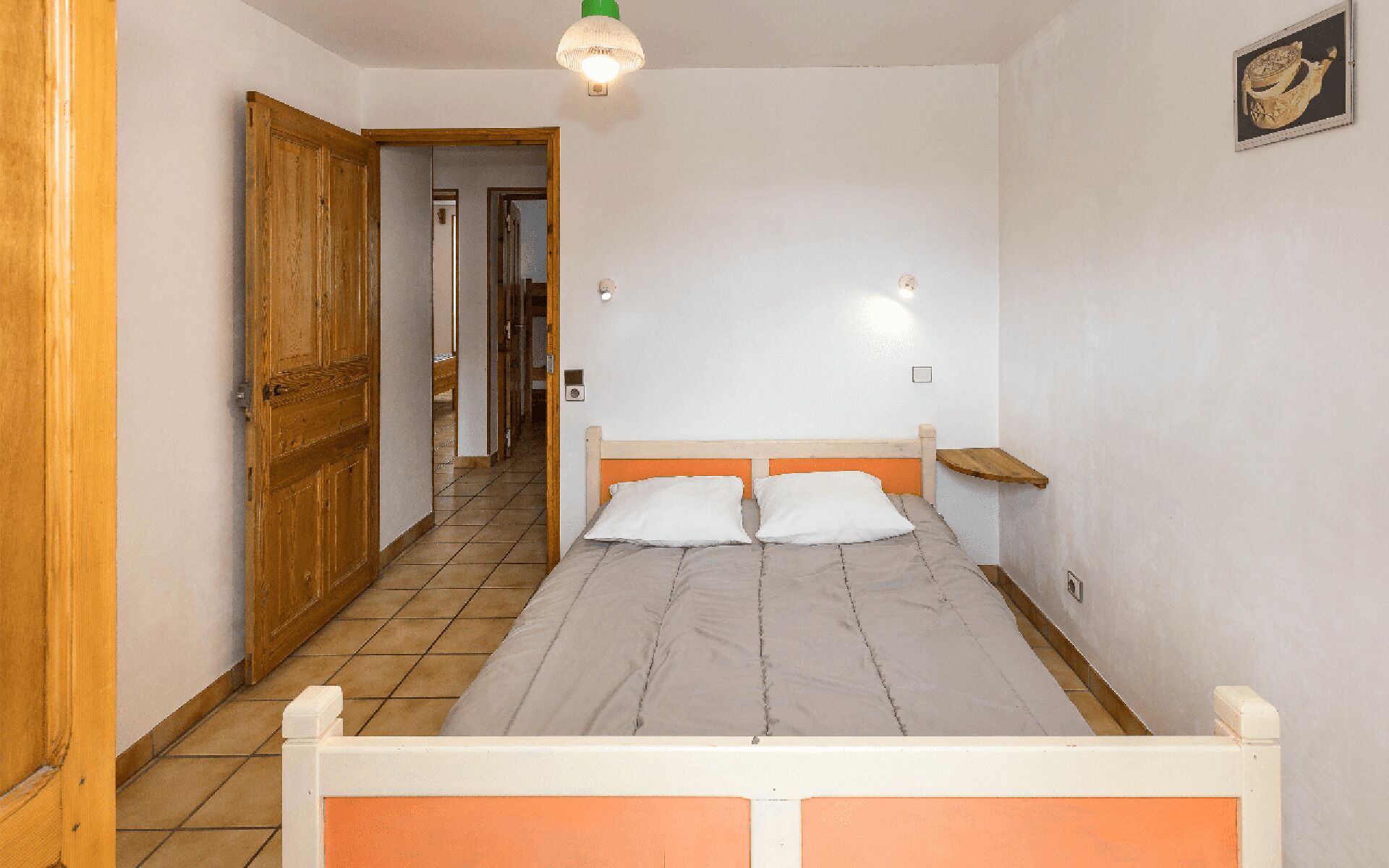 A bedroom with a bed, a wooden door, a hallway, and a light fixture.