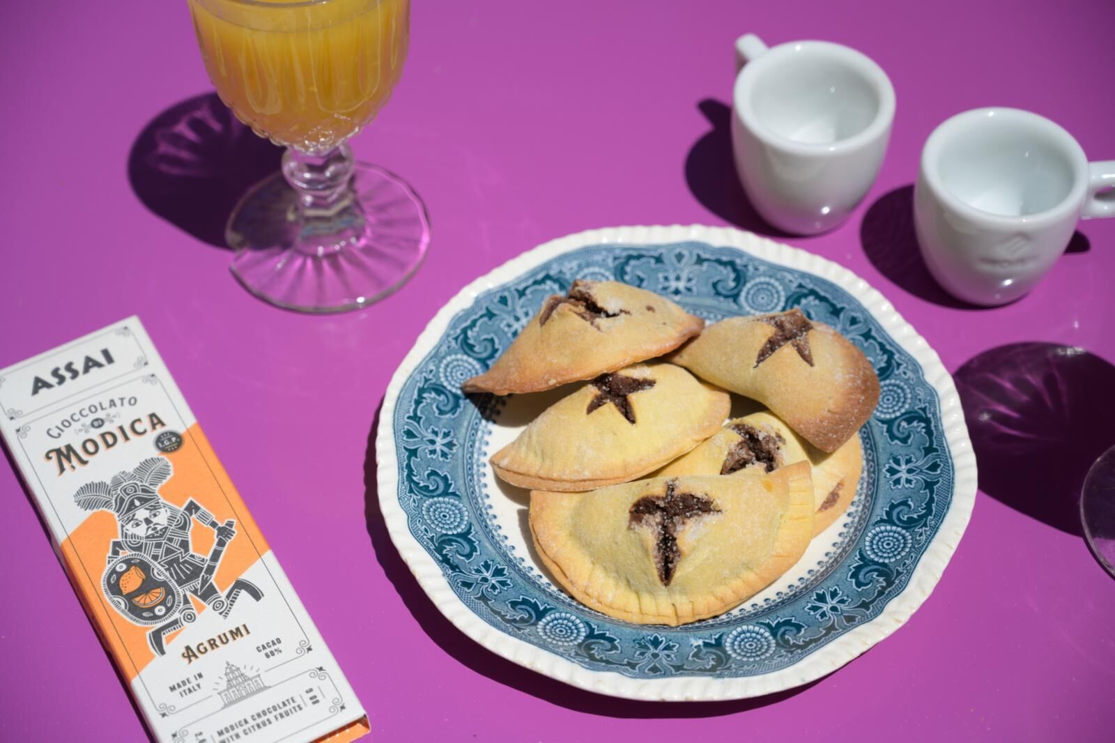 Un piatto di dolci su un tavolo con una scatola di cioccolato di Modica e due tazze bianche.