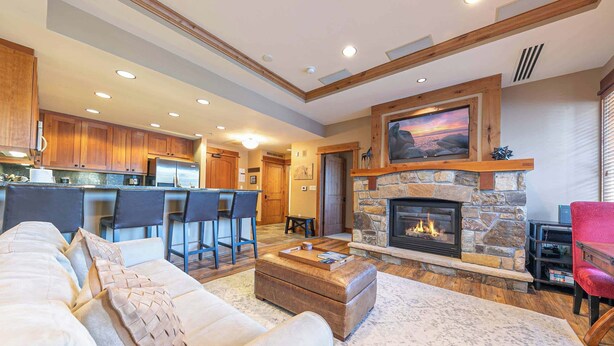 A spacious living room with a stone fireplace, a kitchen in the background, and a dining area with bar stools.