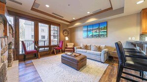A spacious living room with a large window, a fireplace, a sofa, a coffee table, and a dining area with chairs.