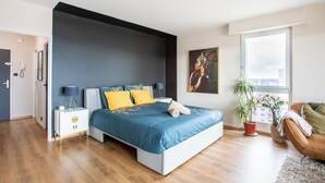Un dormitorio moderno con una cama grande, una mesita de noche, una silla y un ventanal con vistas.