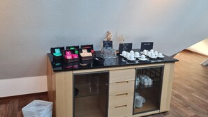 A wooden cabinet with glass doors, a black countertop with coffee cups, and a sign indicating coffee types. - Hotel Pflug (Dornhan)