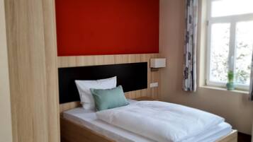 A single bed with a wooden headboard, white bedding, and a green pillow.