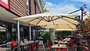 An outdoor dining area with tables and chairs, covered by large umbrellas, and surrounded by potted plants. - Hotel Pflug (Dornhan)