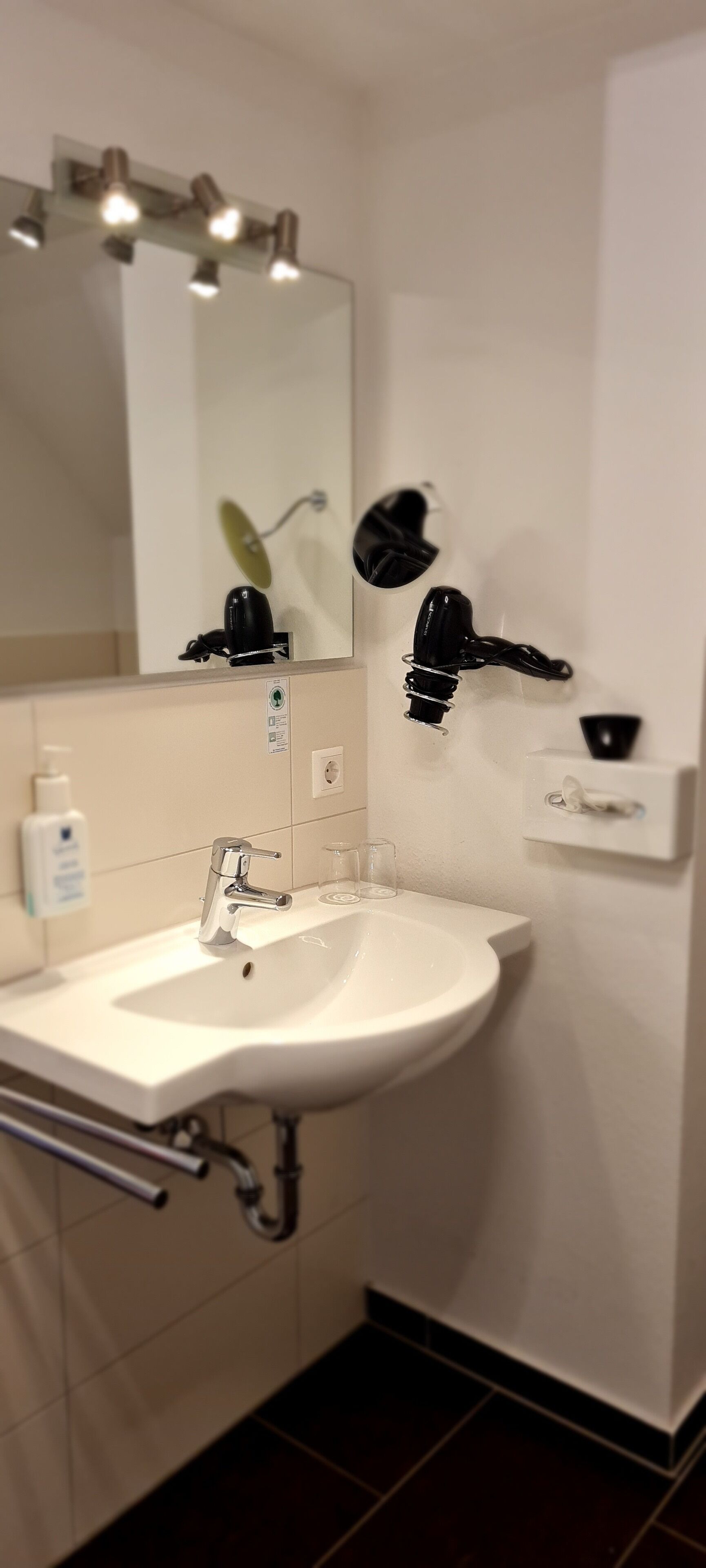 A bathroom with a white sink, a mirror, and a hairdryer mounted on the wall.