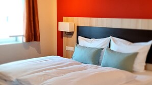 A hotel room with a bed, wooden flooring, a red accent wall, and a window with curtains. - Hotel Pflug (Dornhan)
