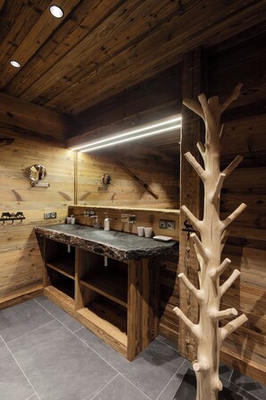 A wooden cabin bathroom with a built-in sink, mirror, and a unique tree-shaped coat rack.