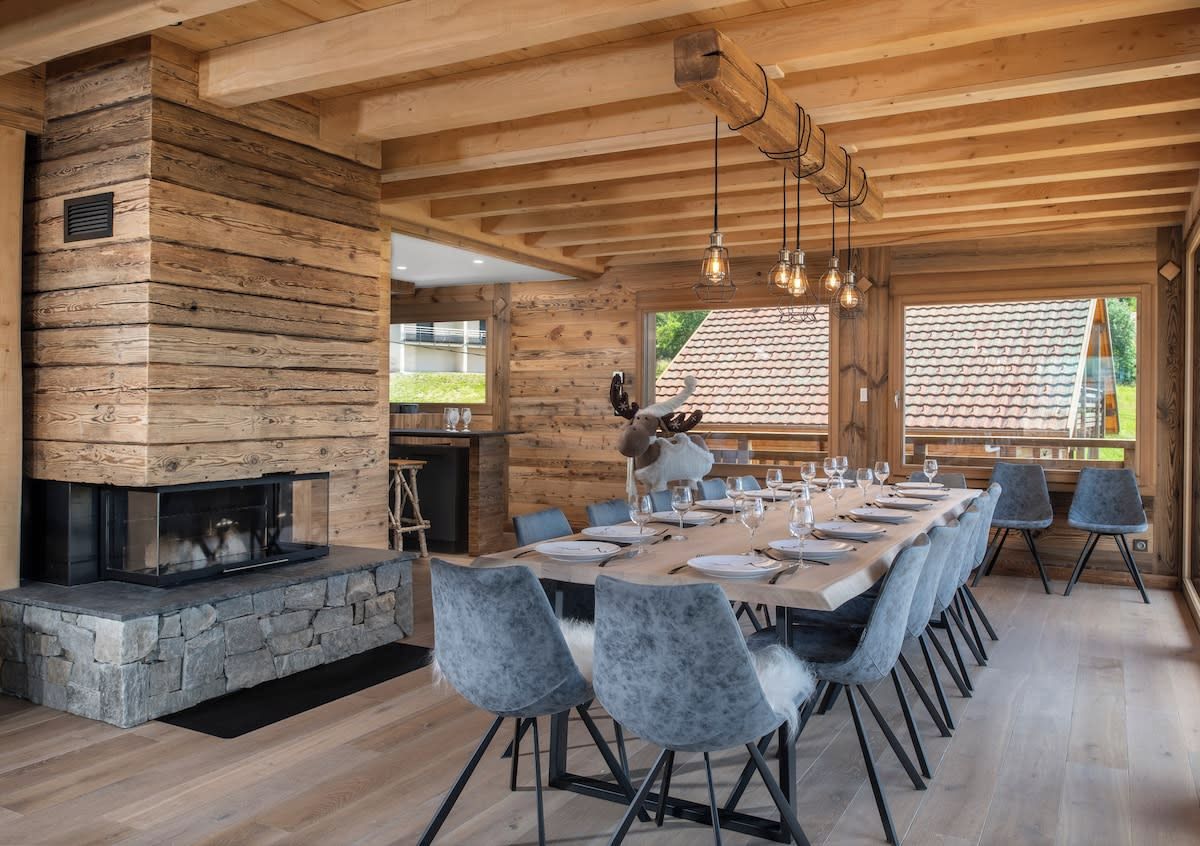 A dining area with a long wooden table, modern chairs, and a stone fireplace.